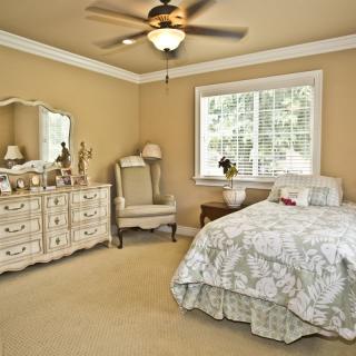 A cozy bedroom featuring a bed with floral bedding, a vintage dresser, and an armchair by the window.