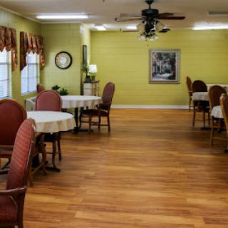 A cozy dining area featuring round tables and comfortable chairs, with green walls and wooden flooring.