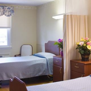 A hospital room with two beds, separated by a curtain, and a nightstand with flowers.