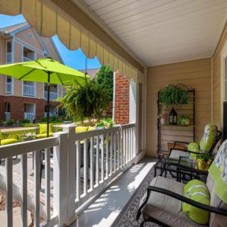 Cozy porch with outdoor seating overlooking a sunny apartment courtyard.