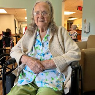 An elderly woman sitting comfortably in her wheelchair, smiling warmly.