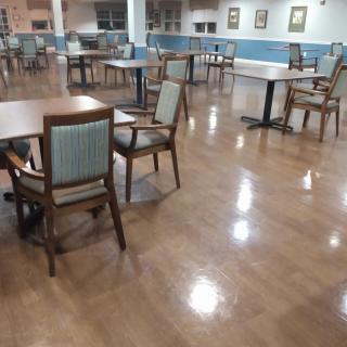 An empty dining area with wooden tables and chairs on a polished floor.