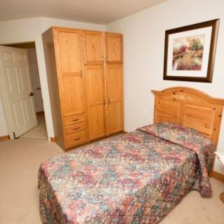A small bedroom with a single bed, wooden wardrobe, and framed artwork on the wall.