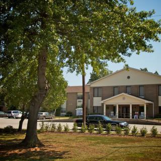 A building with a tree in the foreground and cars parked in the lot on a sunny day.