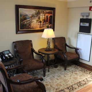 A cozy living area featuring brown upholstered chairs, a lamp on a side table, and a scenic artwork on the wall.