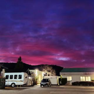 A stunning sunset paints the sky in vibrant shades of purple and pink, framed by buildings and an RV.