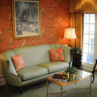 A cozy living room with a pastel green sofa, accompanied by matching decorative pillows and a classic lamp next to a patterned wall.