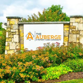 A stone sign for 'The Auberge Community' surrounded by lush greenery.