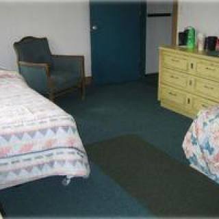 A simple hotel room with two beds, a dresser, and a chair.