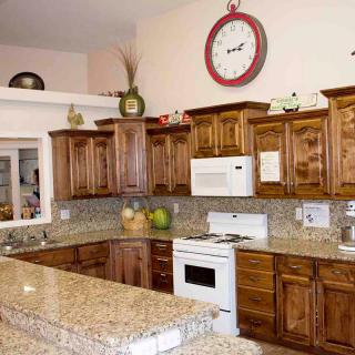 A spacious kitchen featuring wooden cabinets and granite countertops with a large wall clock.