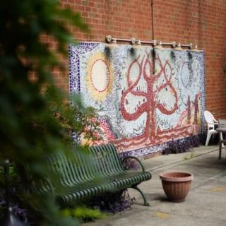 A colorful mural of a tree on a brick wall with a green bench and potted plant nearby.