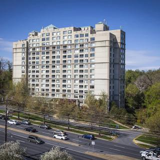 A high-rise apartment building alongside a busy road, surrounded by trees.