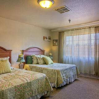 A cozy bedroom featuring two twin beds with matching bedspreads, soft lighting, and natural light streaming through the curtains.