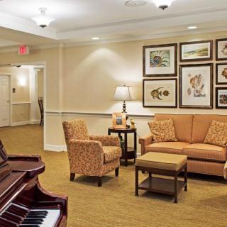 A cozy living room with a sofa and chairs, featuring artwork on the walls and a piano in the corner.
