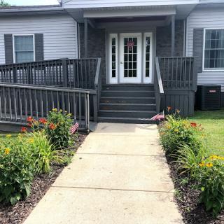 A welcoming entrance with a ramp and pathway lined by flowers leading to the front door of a house.