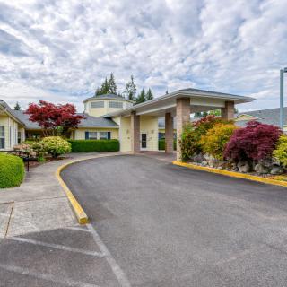 A scenic view of a driveway leading to the entrance of a building surrounded by landscaped greenery.