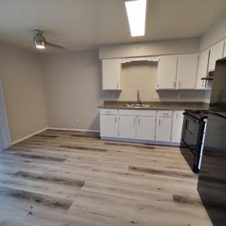 A modern kitchen interior with white cabinets, wood flooring, and stainless steel appliances.