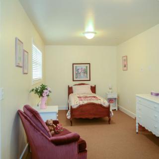 A cozy bedroom with a single bed, a dresser, and a comfortable chair.