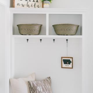A neatly organized entryway with baskets for storage, hooks for hanging items, and a cushion for seating, showcasing minimalist home decor.