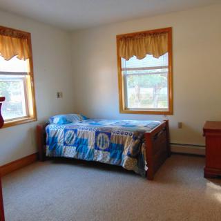 A simple bedroom with a single bed, two windows, and minimal furniture.