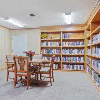 A small library room with wooden shelves filled with books, featuring a table and chairs in the center.