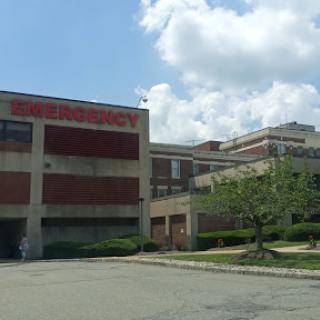 A view of a hospital building featuring the emergency room entrance, set against a partly cloudy sky.