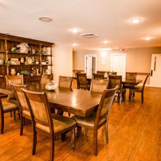 A spacious dining room with wooden tables and chairs, featuring a large bookshelf and warm lighting.