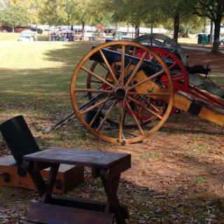 A vintage wagon with wooden wheels displayed in a park, surrounded by trees and grass.