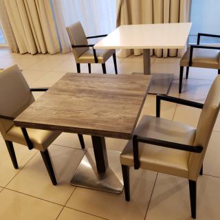 A dining area with square tables and cushioned chairs, arranged in a tiled room.