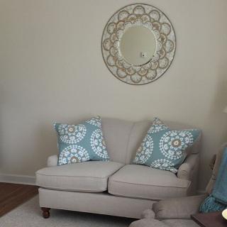 A cozy living room with a neutral sofa and patterned cushions, complemented by a decorative wall mirror.