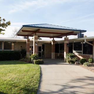 A welcoming entrance to a modern facility, surrounded by green landscaping under a clear blue sky.