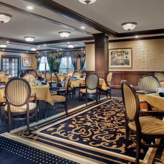 An elegant restaurant dining room with beautifully arranged tables and chairs, adorned with patterned carpet and tasteful lighting.