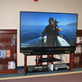 A flat-screen television displaying a fishing program, placed on an entertainment center flanked by bookshelves.