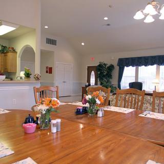 A bright dining room with a wooden table set with flowers and adjacent to a kitchen.