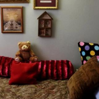 A cozy seating area with a teddy bear, colorful pillows, and framed wall art.