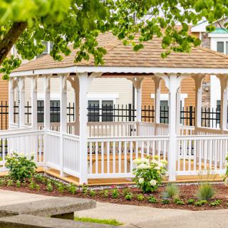 A charming wooden gazebo in a garden setting, surrounded by lush greenery.