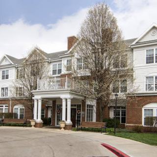 A welcoming residential building with a classic architectural design, surrounded by trees against a partly cloudy sky.