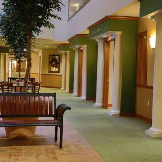 A spacious hallway featuring columns, green walls, a wooden bench, and artwork on display.