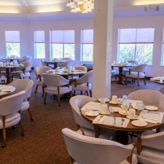 An elegant dining room with neatly arranged tables and chairs, softly lit by natural light from large windows.