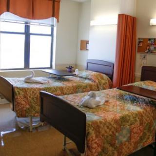 A spacious hospital patient room with two beds, featuring colorful bedding and natural light from the window.