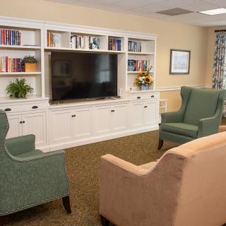 A cozy living room with a TV, bookshelves, and comfortable seating.