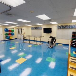 A well-lit physical therapy room with various exercise equipment and colorful gym mats.