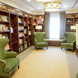 A cozy library reading room with green armchairs and bookshelves lining the walls.