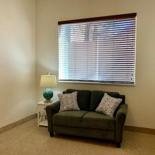 A cozy corner in a living room featuring a green sofa, decorative pillows, and a lamp beside a window.