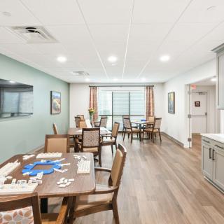 A communal dining area with tables and chairs, featuring a television and games on the tables.