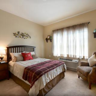 A cozy bedroom with a neatly made bed, armchair, and soft lighting.