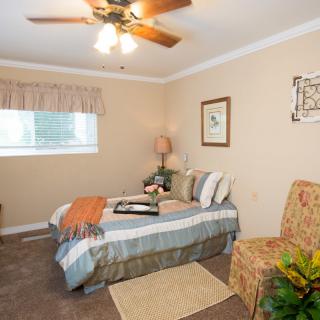 A cozy bedroom with a neatly made bed, ceiling fan, and warm lighting.
