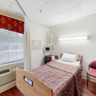 A cozy hospital patient room featuring a bed, window, and chair.