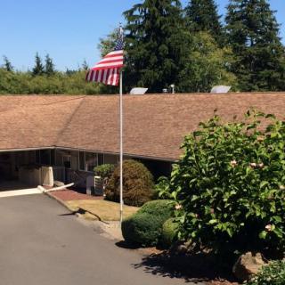 A building with an American flag in front, surrounded by greenery under a clear blue sky.