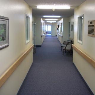 A long, clean hospital corridor with fluorescent lights and chairs along the walls.